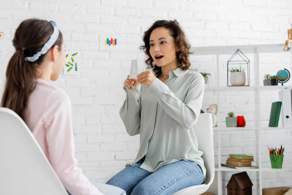 Speech therapist holding letter a near blurred pupil in consulting room