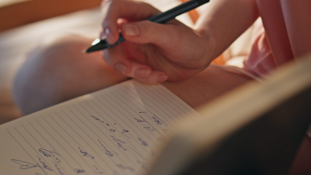 closeup of hand writing goals down in their NDIS goal setting notebook