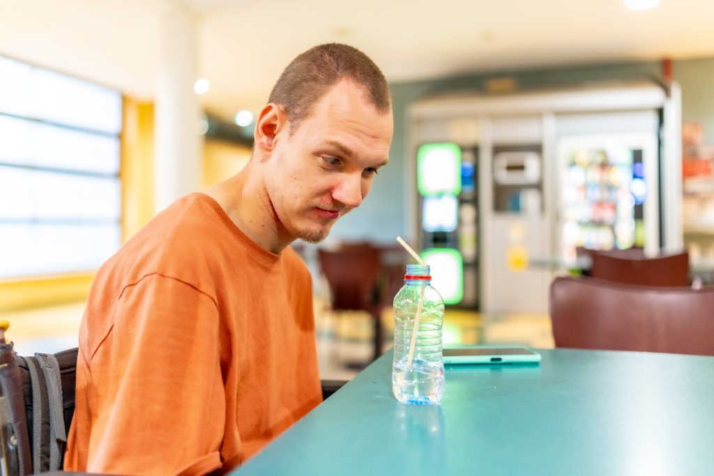Man with cerebral palsy drinking water in a coworking cafeteria after setting clear NDIS goals about maintaining work