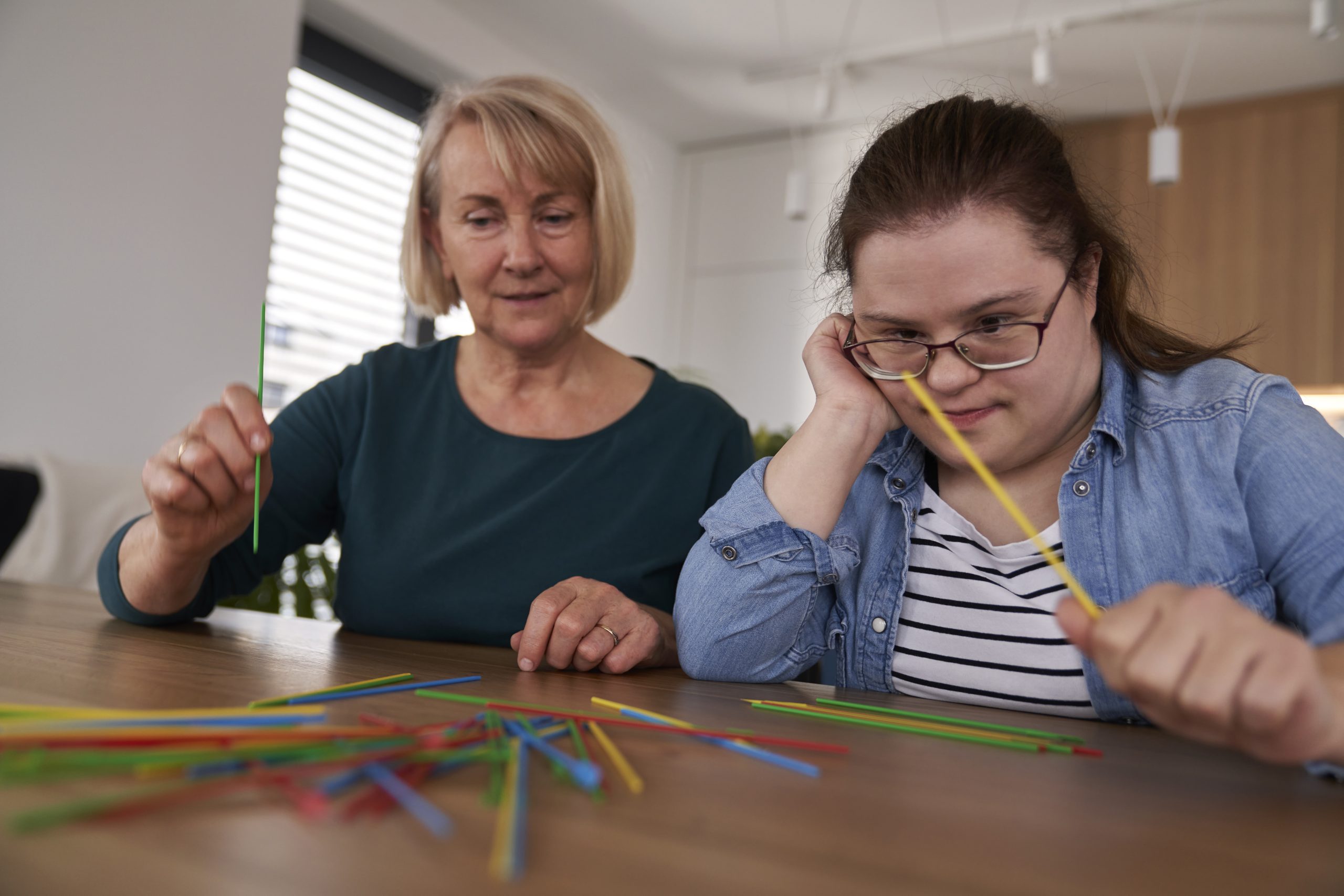 Down syndrome woman and her mother playing pick up sticks at home